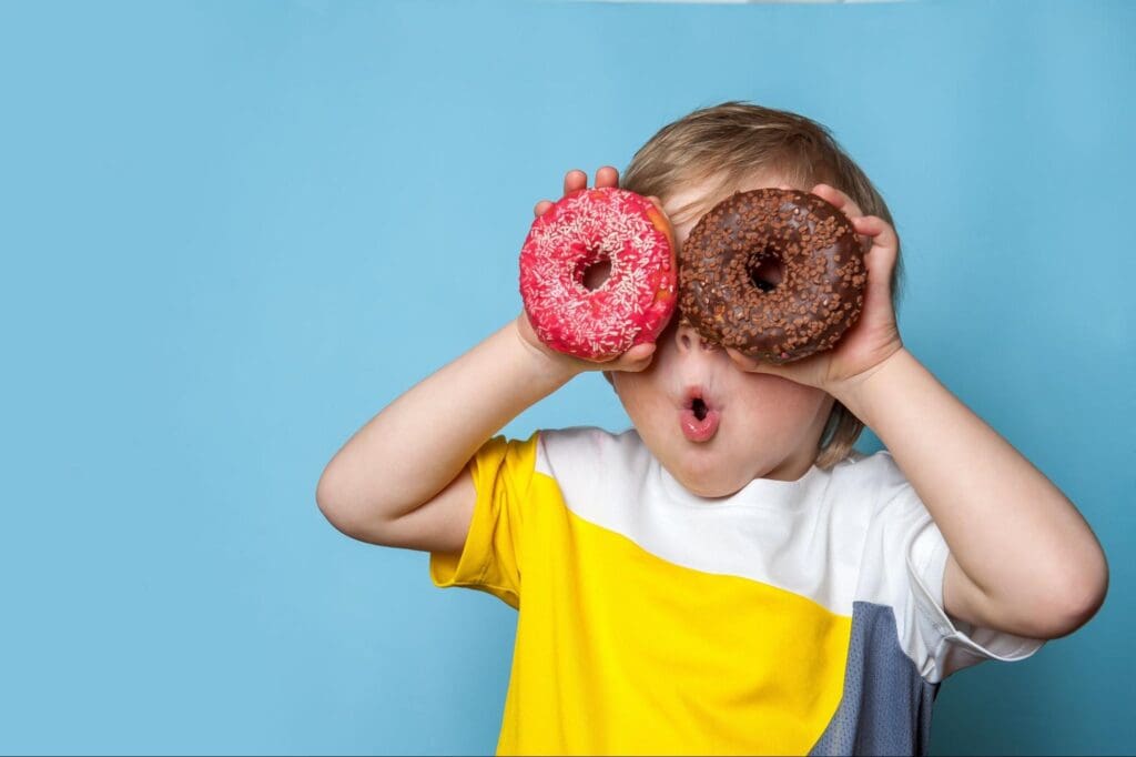 Child holding donuts over eyes, making a playful face