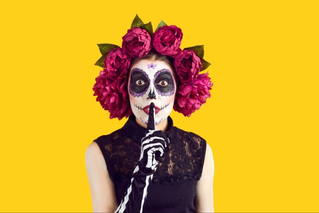 Woman in Dia de los Muertos makeup with pink roses on yellow background
