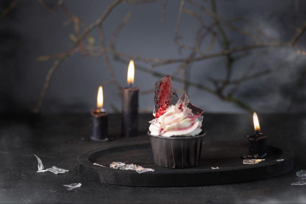 Gothic style cupcake with white frosting and red jam on a dark plate with candles