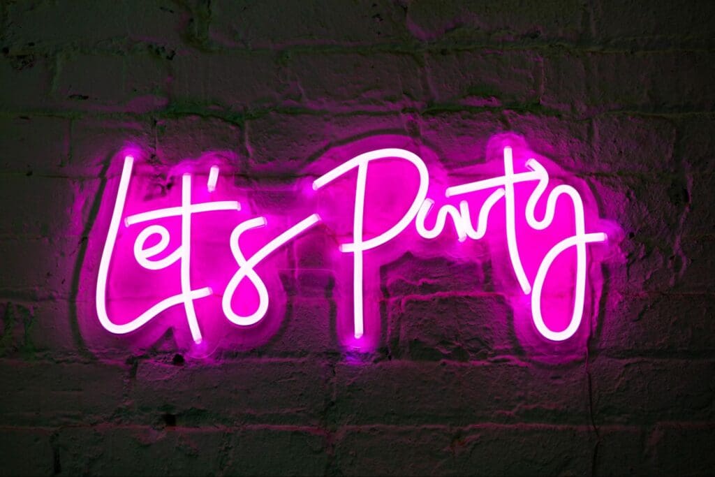 Neon sign with the words 'Let's Party' in pink on a brick wall