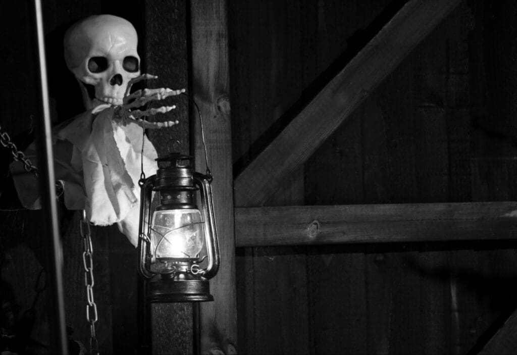 Black and white image of a skeleton holding a lantern in a spooky setting