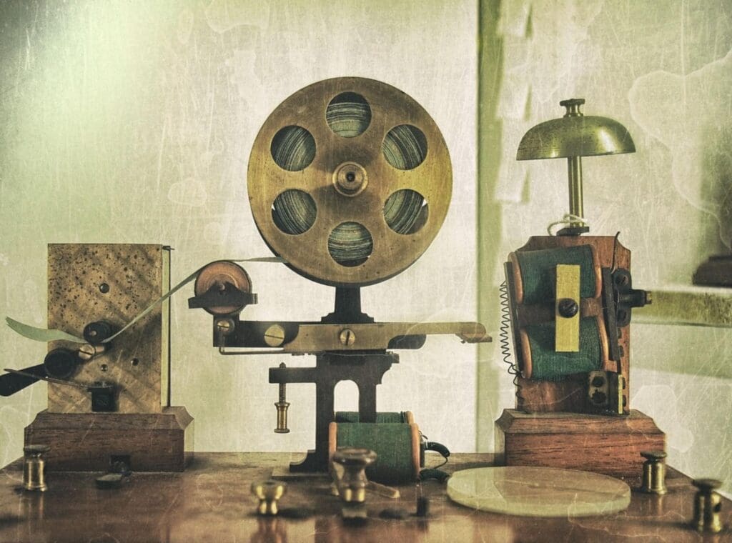 Vintage film projection equipment setup with reels, projectors, and other mechanisms displayed on a wooden table, evoking a historical film editing room atmosphere.