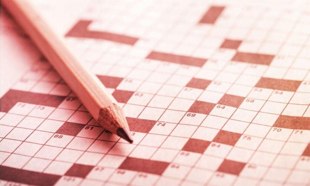 Close-up of a crossword puzzle with a sharpened pencil, emphasizing the grid filled with numbers and empty squares in a sepia tone."