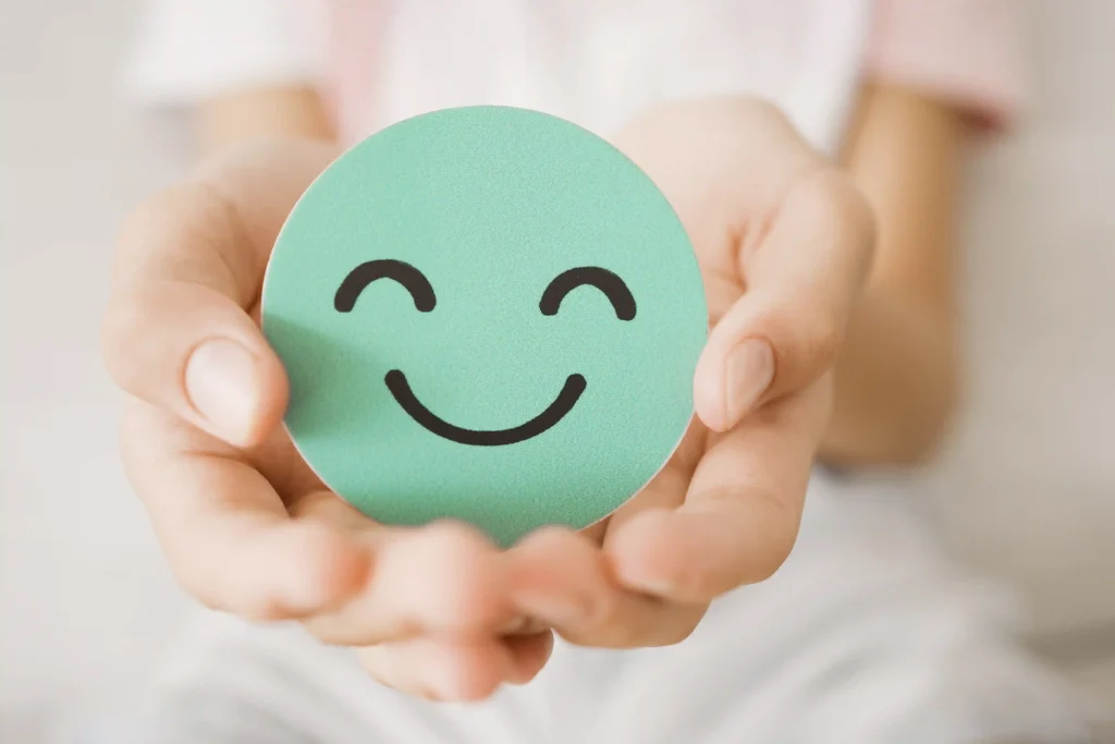 Hands holding a round smiley face icon, representing wellness and positivity.