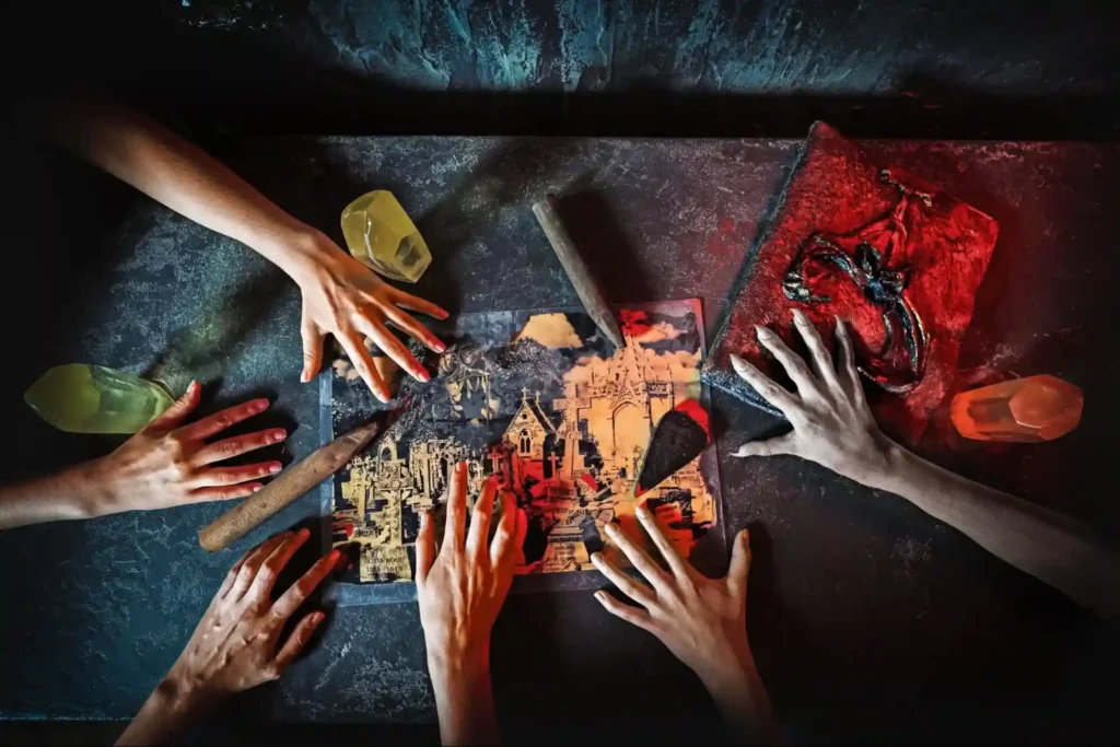 A group of hands working together to solve a puzzle on a dimly lit table in an escape room, featuring mysterious objects and glowing crystals.