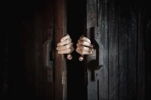 Hands pulling open a dark wooden door, revealing the entrance to an escape room with a mysterious atmosphere.