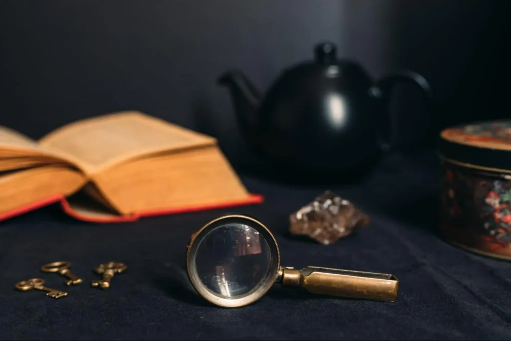 A magnifying glass, old-fashioned keys, and an open book on a dark table, hinting at clues in an escape room setting.