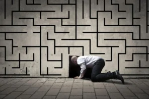 Man crawling into a small opening in a maze-like wall, symbolising problem-solving, confinement, and navigating challenges, often associated with escape rooms.