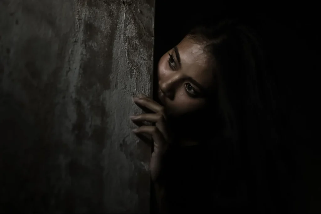 A person peeking nervously around a dark wall, illustrating fear or suspense.