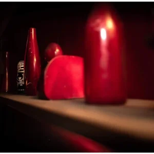 Collection of red objects on a dimly lit shelf, adding mystery to the decor in Kellar's Magic Emporium escape room.